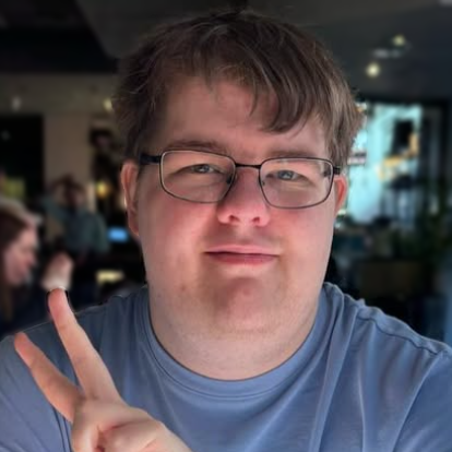 Side-on portrait photo of my face, mouth slightly open smiling wearing glasses with brown hair in a light blue polo shirt